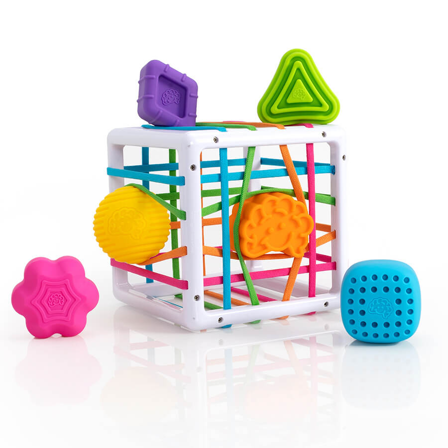 Fat Brain Toys InnyBin – sensory shape‑exploration cube with six chunky, textured blocks (cube, diamond, sphere, triangle, flower, logo) and elastic bands for frustration‑free fine motor play