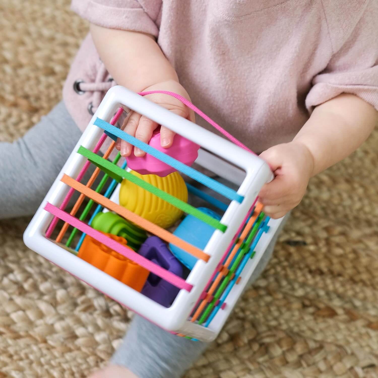 Fat Brain Toys InnyBin – sensory shape‑exploration cube with six chunky, textured blocks (cube, diamond, sphere, triangle, flower, logo) and elastic bands for frustration‑free fine motor play