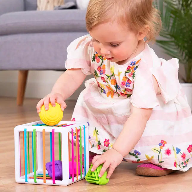 Fat Brain Toys InnyBin – sensory shape‑exploration cube with six chunky, textured blocks (cube, diamond, sphere, triangle, flower, logo) and elastic bands for frustration‑free fine motor play