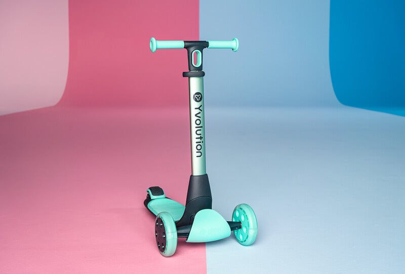YGlider Nua green 2‑in‑1 foldable lean‑to‑steer scooter – lightweight kids’ scooter with adjustable arc‑folding handlebar, LED front wheels, wide rear wheel and wall‑mount accessory