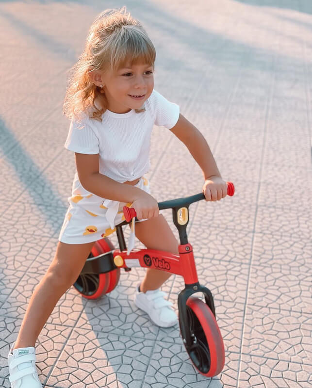 Velo Junior red balance bike for toddlers – two‑stage no‑pedal training bike with dual rear wheels, adjustable seat and handlebars, lightweight aluminum frame and puncture‑proof wheels